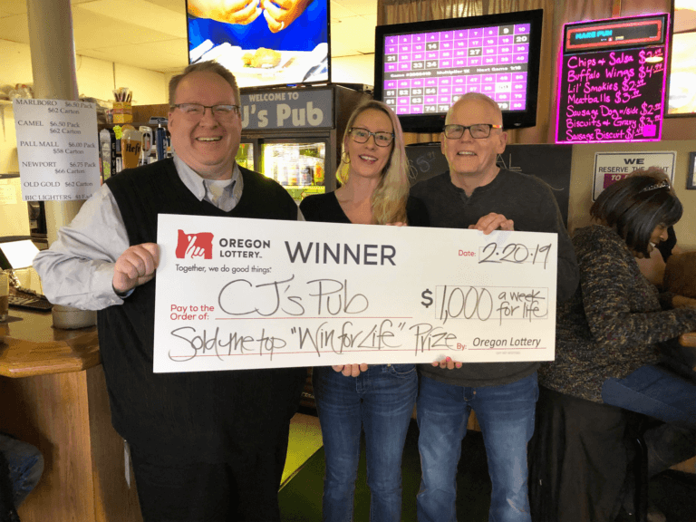 Three people posing with oversized check awarded CJ's pub Lottery commission