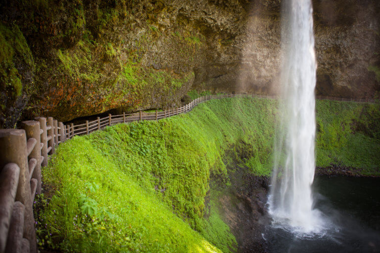 A fence marks a trail leading behind a waterfall