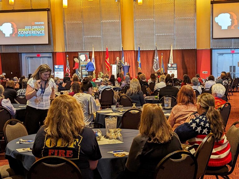 Women in a large conference room attend a speech