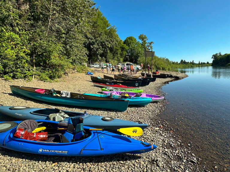 Colorful kayaks line the short of the river in preparation for launching.