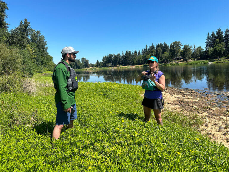 Two people standing in vegetation at the side of the river.