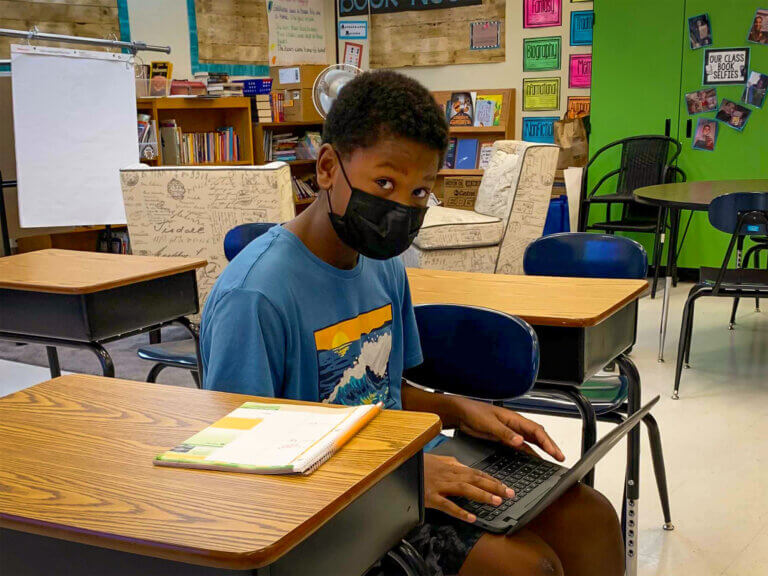 A young boy works on a laptop at a student desk.