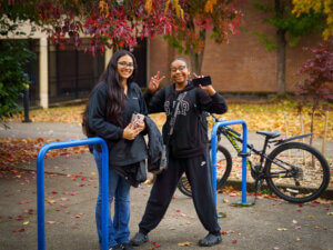 Two girls pose outside a school near a bike rack.